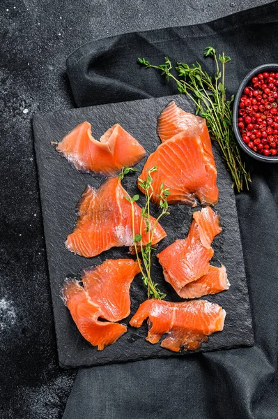 Salted salmon slices with pepper and thyme. Organic fish. Black background. Top view.