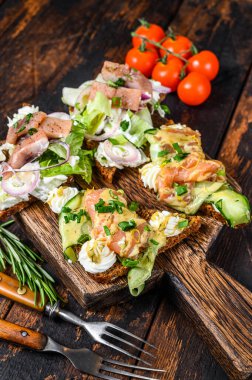 Tütsülenmiş somon balığı ve krem peynirli ringa balığı sandviçi ve salata. Koyu ahşap arka plan. Üst görünüm.