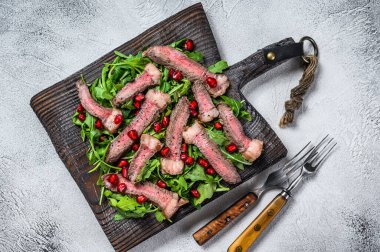 Köy kesim tahtasının üzerinde roka yapraklı ızgara biftek salatası. Beyaz arka plan. Üst görünüm.