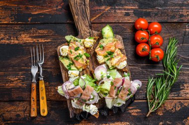 Tütsülenmiş somon balığı ve krem peynirli ringa balığı sandviçi ve salata. Koyu ahşap arka plan. Üst görünüm.