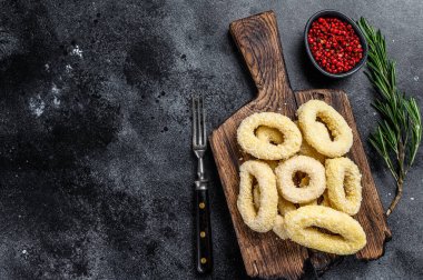 Kesme tahtasındaki ekmek kırıntıları içinde çiğ kalamar halkaları. Siyah arka plan. Üst Manzara. Boşluğu kopyala.