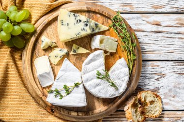 Yuvarlak ahşap kesim tahtasında çeşitli peynirler. Camembert peyniri, peynir ve üzümlü mavi peynir. Beyaz ahşap arka plan. Üst görünüm.