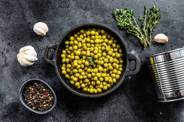 Dökme demir kasede yeşil bezelyeler. Konserve yiyecekler. Siyah arka plan. Üst görünüm.