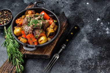 Koyu kırsal kesim tahtasındaki tencerede et güveci. Siyah arka plan. Üst Manzara. Boşluğu kopyala.