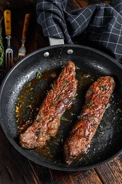 Grilled flank Steak in a pan. Dark wooden background. Top view.