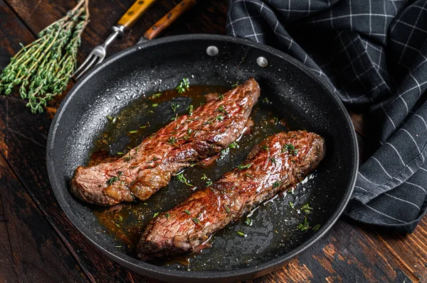 Grilled flank Steak in a pan. Dark wooden background. Top view.