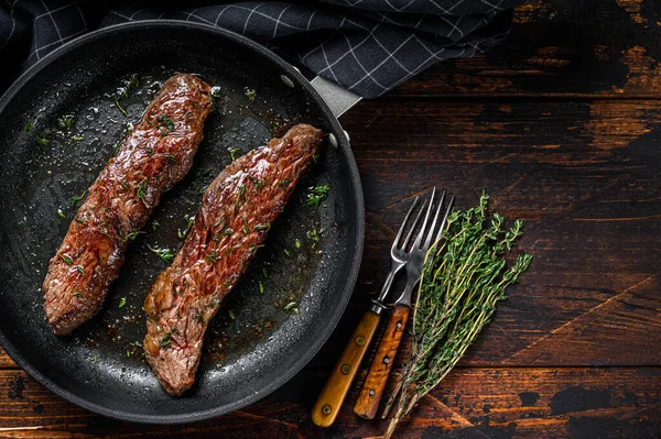 Grilled flank Steak in a pan. Dark wooden background. Top view. Copy space.