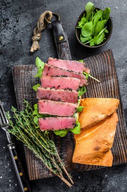 Baget ton balıklı biftekli sandviç ve yanında roka. Siyah arka plan. Üst görünüm.