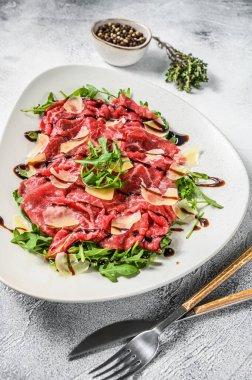Parmesan peyniri ve roka ile beyaz tabakta sığır eti carpaccio. Gri arka plan. Üst görünüm