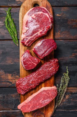 Assortment of raw beef steaks Tenderloin fillet mignon, ribeye, Striploin or new york, skirt, machete. Wooden dark background. Top view. clipart