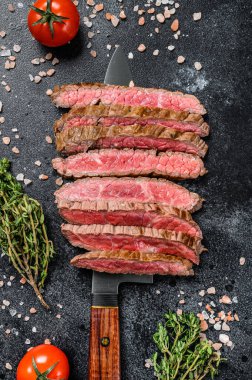 Izgara ve dilimlenmiş demir gibi az pişmiş biftek. Mermer sığır eti. Siyah arka plan. Üst görünüm.