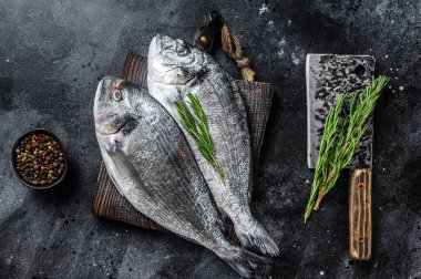 Kesme tahtasındaki çiğ deniz kepekli dorado balığı. Siyah arka plan. Üst görünüm.