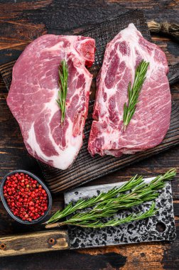 Et satırıyla kesme tahtasının üzerinde otlu çiğ domuz filetosu bifteği. Koyu ahşap arka plan. Üst görünüm.