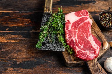 Çiğ Black Angus dana eti rulo bifteği bir kesme tahtasında satırla birlikte. Koyu ahşap arka plan. Üst Manzara. Boşluğu kopyala.