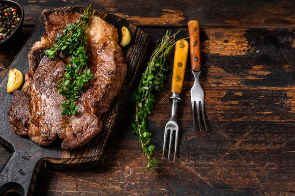 Grilled Chuck eye roll beef meat steak on a cutting board. Dark wooden background. Top view. Copy space.