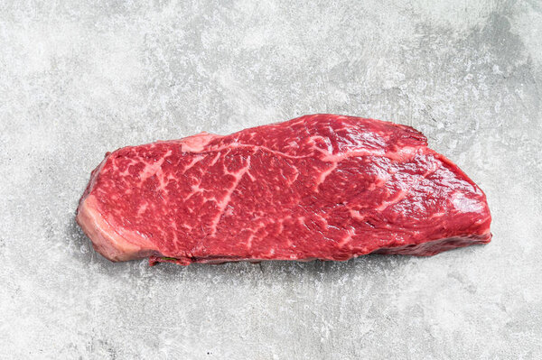 Сырой стейк из стриплоина, мраморная говядина. Серый фон. Вид сверху.
