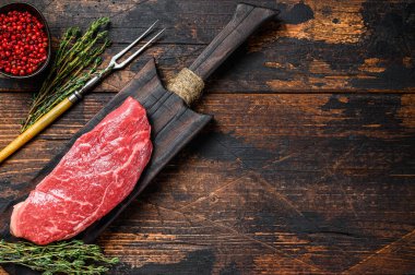 Kesme tahtasındaki çiğ Striploin bifteği, mermer sığır eti. Karanlık ahşap arka plan. Üst Manzara. Boşluğu kopyala.