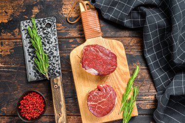 Kesme tahtasının üzerinde çiğ biftek fileto fileto. Karanlık ahşap arka plan. Üst görünüm.