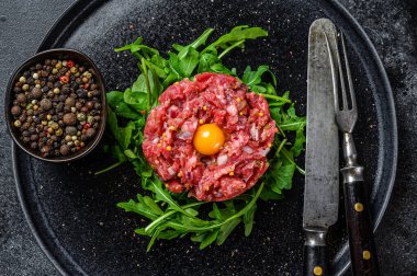 Siyah arka planda, siyah taştan bir tabakta servis edilen bıldırcın yumurtalı biftek tartartarı. Üst görünüm.