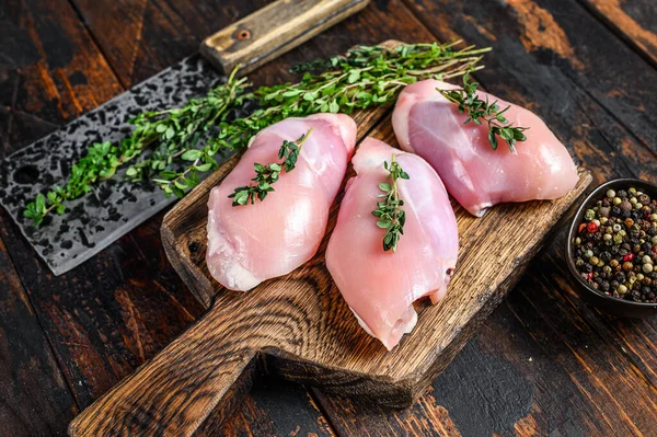 Raw Chicken skinless thigh fillet on a wooden cutting board. Black background. Top view.