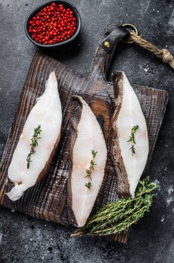 Tahta bir tahtanın üzerinde çiğ taze halibut balığı bifteği. Siyah arka plan. Üst görünüm.