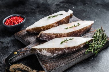 Tahta bir tahtanın üzerinde çiğ taze halibut balığı bifteği. Siyah arka plan. Üst görünüm.