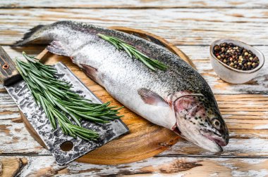 Ağaç bir tahtada, biberiye ve satırla gökkuşağı alabalığı. Beyaz ahşap arka plan. Üst görünüm.