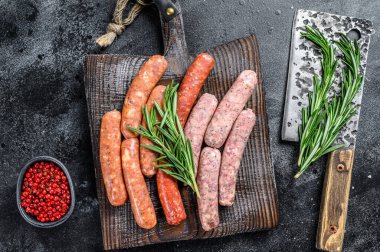 Tahta bir kesme tahtasının üzerinde çiğ sucuk çeşitleri. Siyah arka plan. Üst görünüm.