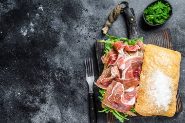 Ciabatta ekmeğinde Iberico Jamon jambonlu sandviç. Siyah arka plan. Üst Manzara. Boşluğu kopyala.