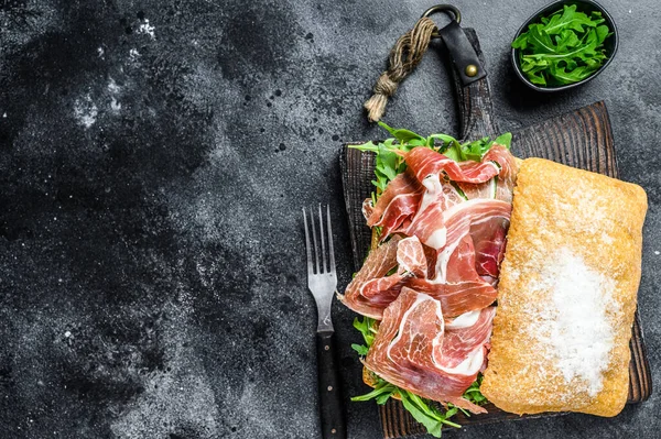 Ciabatta ekmeğinde Iberico Jamon jambonlu sandviç. Siyah arka plan. Üst Manzara. Boşluğu kopyala.