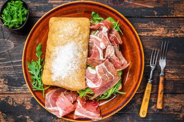 İspanyol bocadillo de jamon, ciabatta ekmekli serrano jambonlu sandviç roka. Koyu ahşap arka plan. Üst görünüm.