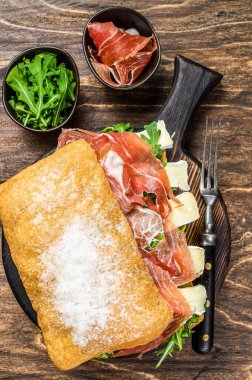 Jamon jambonlu sandviç, yanında roka ve peynirli peynirli ciabatta ekmeği. Ahşap arka plan. Üst görünüm.