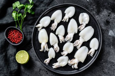 Biberiye ve maydanozlu çiğ mürekkep balığı. Siyah arka plan. Üst görünüm.