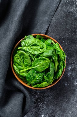 Tahta bir kasede taze ıspanak yaprakları. Siyah arka plan. Üst görünüm.