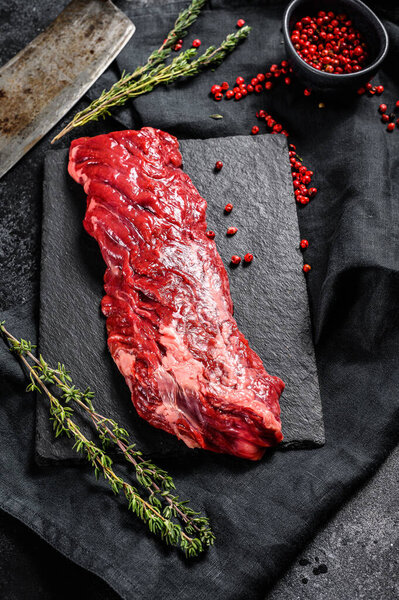 Raw marbled beef steak with pink pepper and thyme. Black background. Top view.