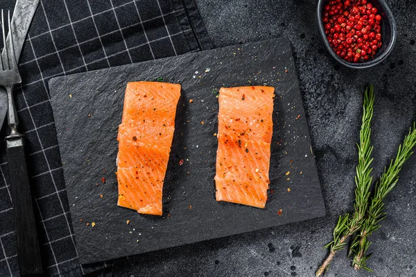 Taş bir tahtanın üzerinde fileto somon bifteği. Siyah arka plan. Üst görünüm.