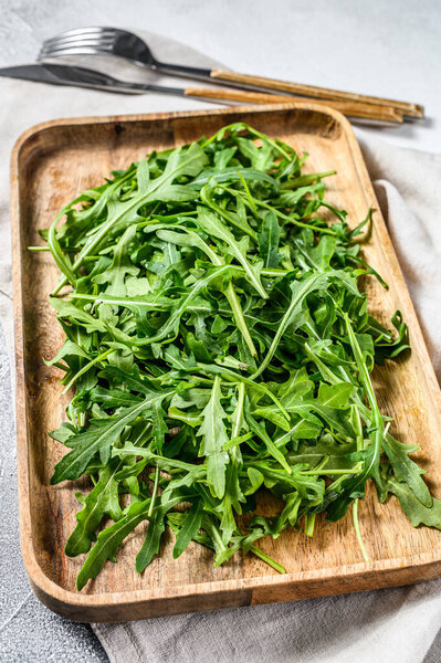 Fresh arugula salad in a wooden bowl. Gray background. Top view.