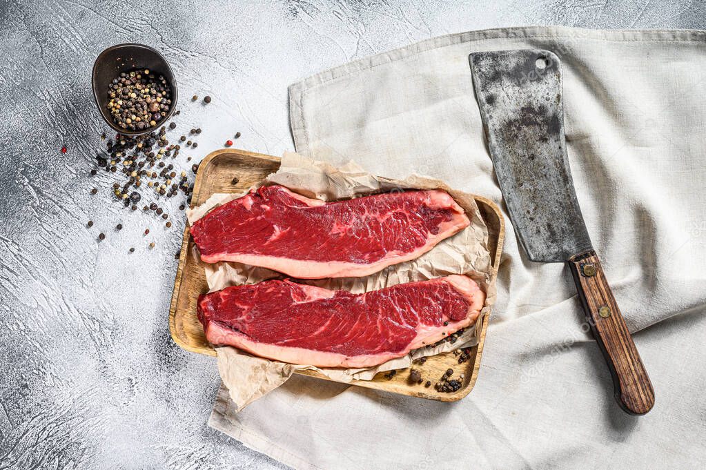 Raw sirloin steak on a wooden tray with a meat cleaver. Marble beef. Gray background. Top view.