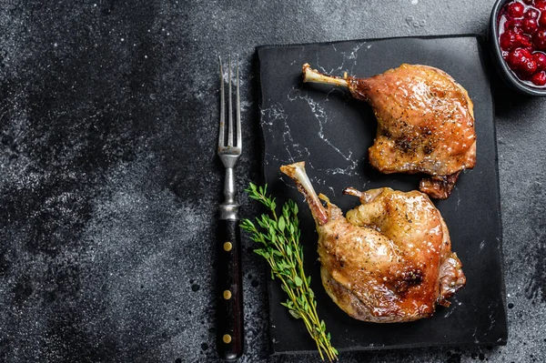 Roasted duck leg confit with cranberrie sauce. Black background. top view. Copy space.