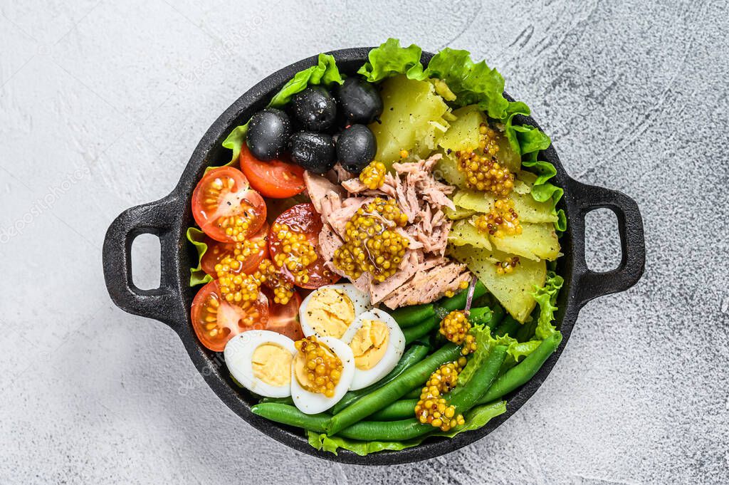 Gourmet nicoise salad with vegetables, eggs, tuna and anchovies in a pan. White background. top view.