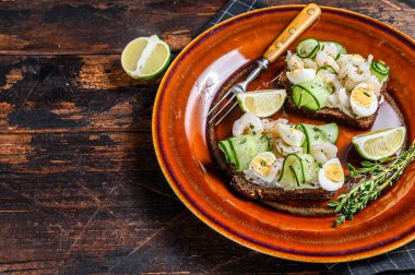 Karidesli İskandinav sandviçi, karides, bıldırcın yumurtası ve çavdar ekmeğine salatalık. Karanlık ahşap arka plan. Üst Manzara. Boşluğu kopyala.