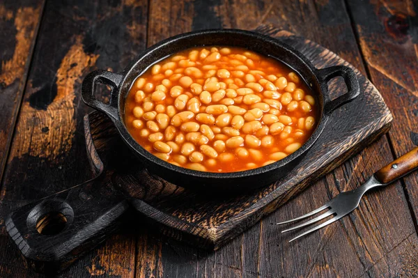 Beans in tomato sauce in a pan. Dark wooden background. top view.