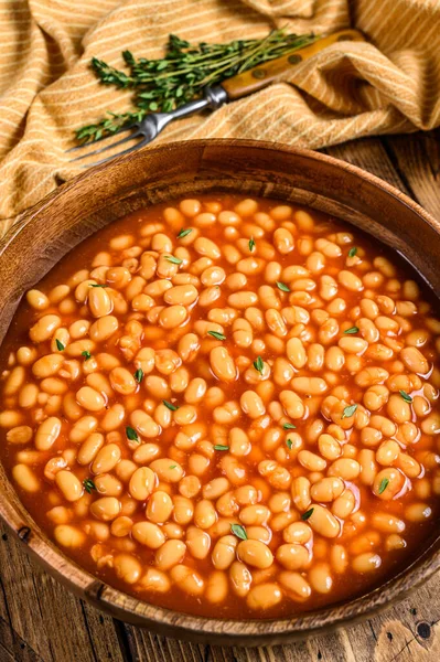 White beans in tomato sauce in a wooden plate. wooden background. top view.