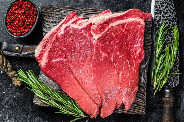 Raw fresh beef meat round steak with herbs and spices. Black background. Top view.