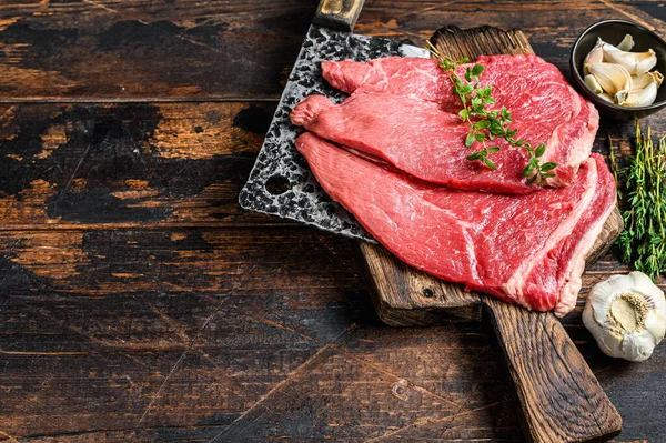 Çiğ dana eti, pirzola. Kesme tahtasının üzerinde, koyu ahşap arka planda. Üst Manzara. Boşluğu kopyala.