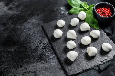 Üzerinde fesleğen yaprağı ve pembe biber olan taş bir tahtada mini mozzarella peyniri topları. Siyah arka plan. Üst Manzara. Boşluğu kopyala.