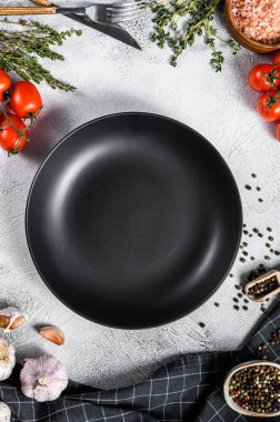 Taze çiğ sebze ve sebzelerin ortasında siyah boş bir tabak. Sağlıklı, temiz yemek, vejetaryen, diyet yemek konsepti. Beyaz arka plan. Üst Manzara. Boşluğu kopyala.