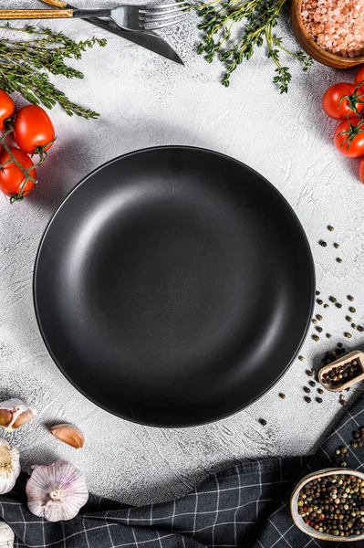 Taze çiğ sebze ve sebzelerin ortasında siyah boş bir tabak. Sağlıklı, temiz yemek, vejetaryen, diyet yemek konsepti. Beyaz arka plan. Üst Manzara. Boşluğu kopyala.