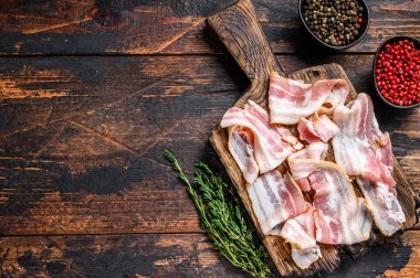Tahta kesme tahtasında çiğ domuz pastırması dilimleri. Koyu ahşap arka plan. Üst Manzara. Boşluğu kopyala.