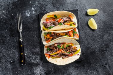 Biftek, soğan, domates ve tatlı biberli Meksika taco kabuğu. Siyah arka plan. Üst görünüm.